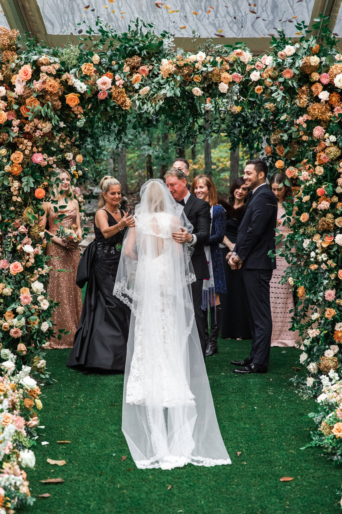 Eye-catching oversized chuppah overflowing with fall florals featuring dahlias, garden roses, rain tree pods, and fall greenery. Autumnal hues of terra cotta, dusty pink, copper, and yellow create this statement wedding piece. Designed by Rosemary and Finch in Nashville, TN.