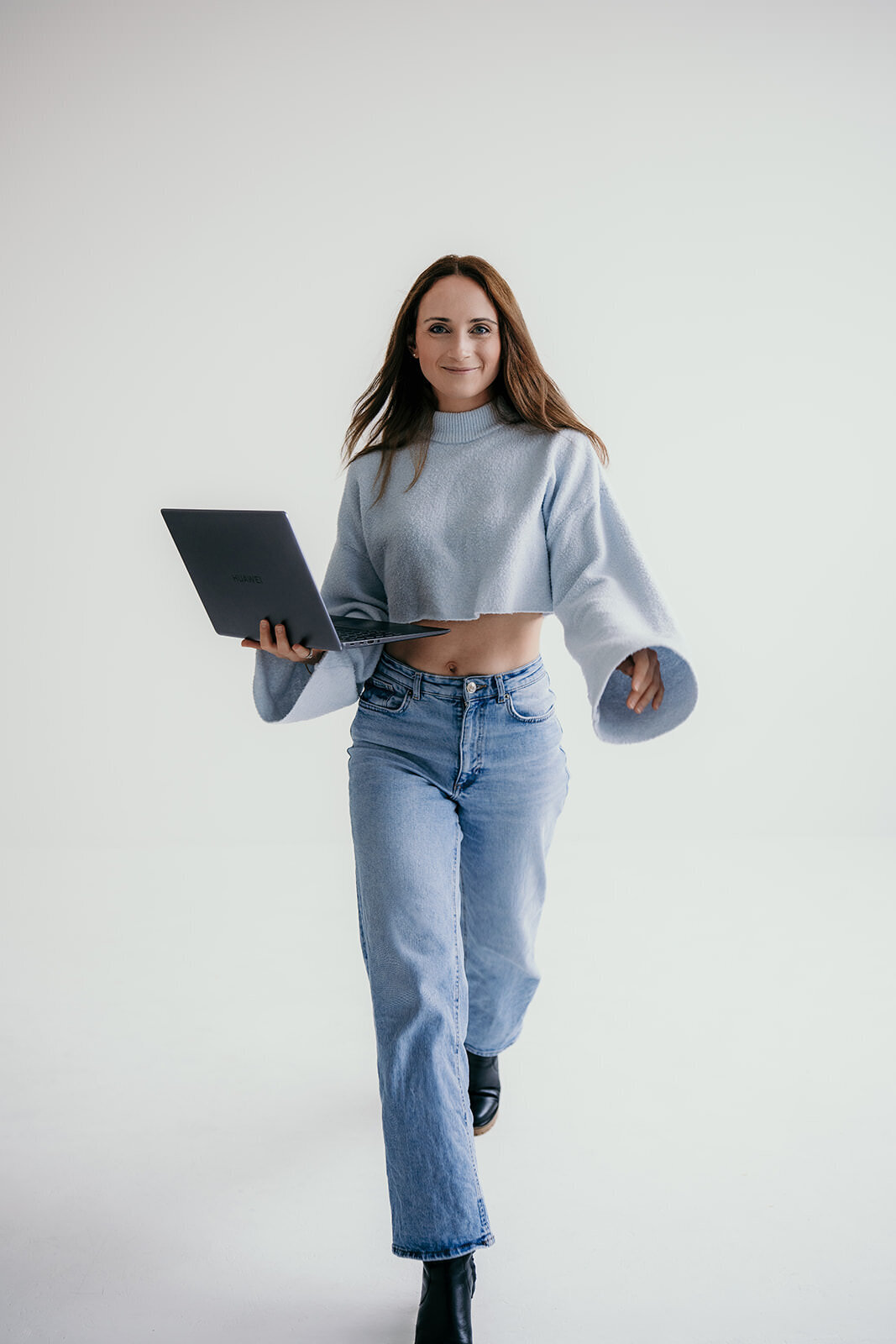 Woman walking towards the camera with a laptop in her hand.