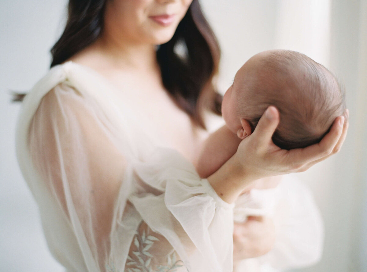 Mother cradling newborn against neutral backdrop, Bay Area newborn photographer session.