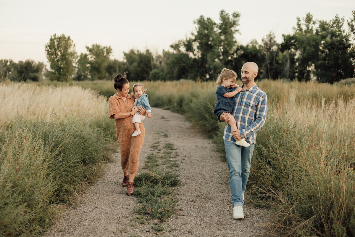 family of four, mom and dad each holding daughter while walking towards alexis adkins photo during family session in longmont colorado