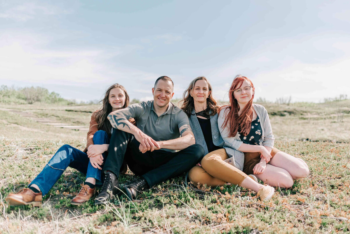 Family of 4 sit in some grass. 