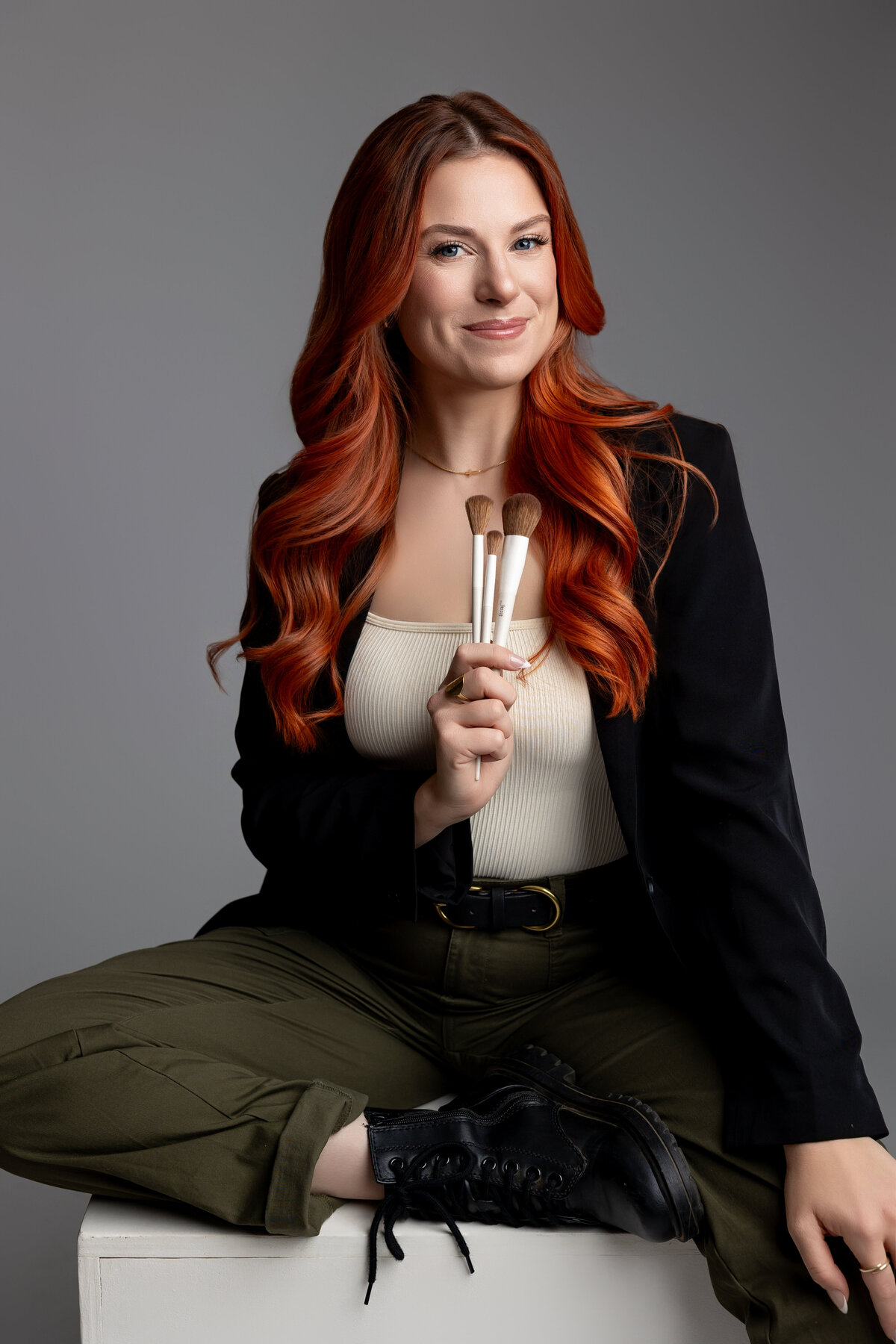 Professional woman with red hair applying lipstick while seated at a studio desk. Photograph by Yucaipa branding photographer Kaitlyn Dawn Photography.