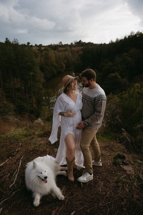 Couple surplombant la vallée accompagné de leur chien. Robe blanche légère pour elle et pull nordique pour lui. Shooting photo grossesse en pleine nature par Kamescop.
