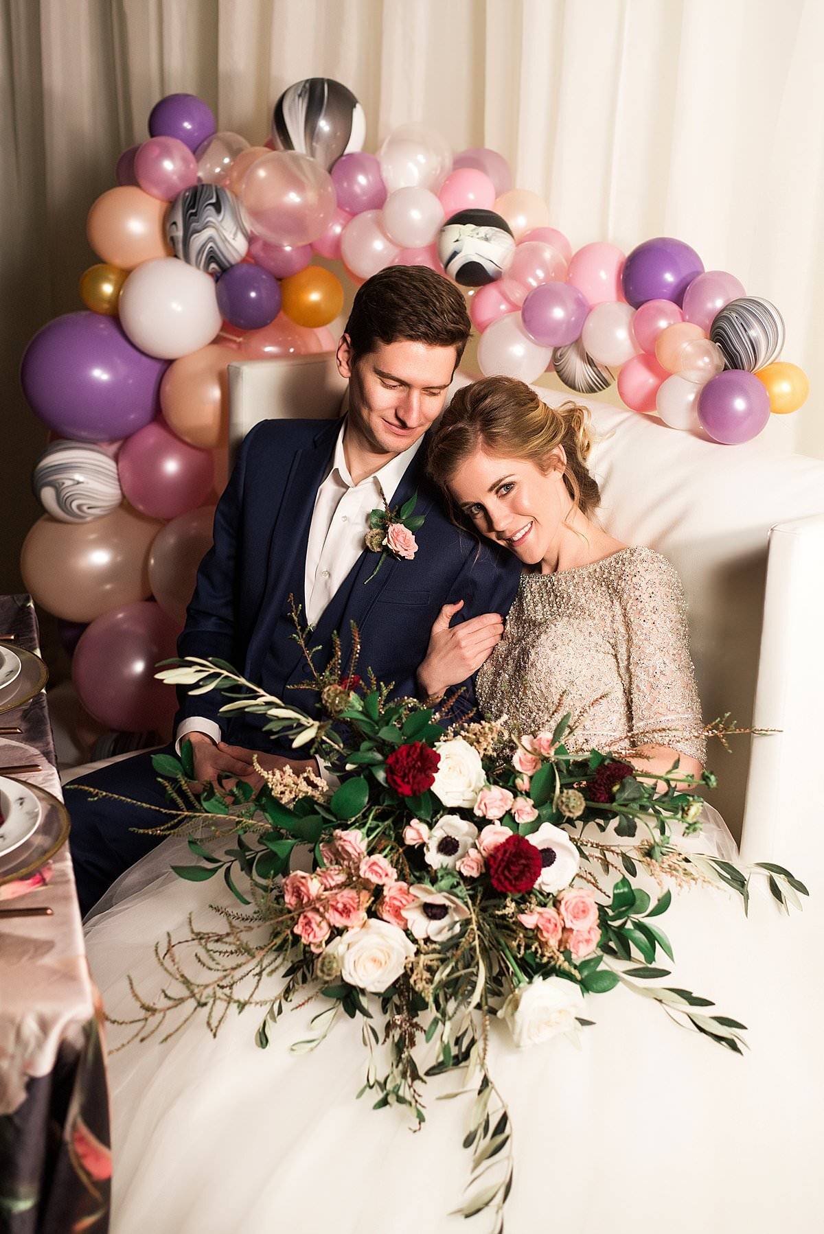 Couple sitting together on couch with balloon instillation and large wedding bouquet