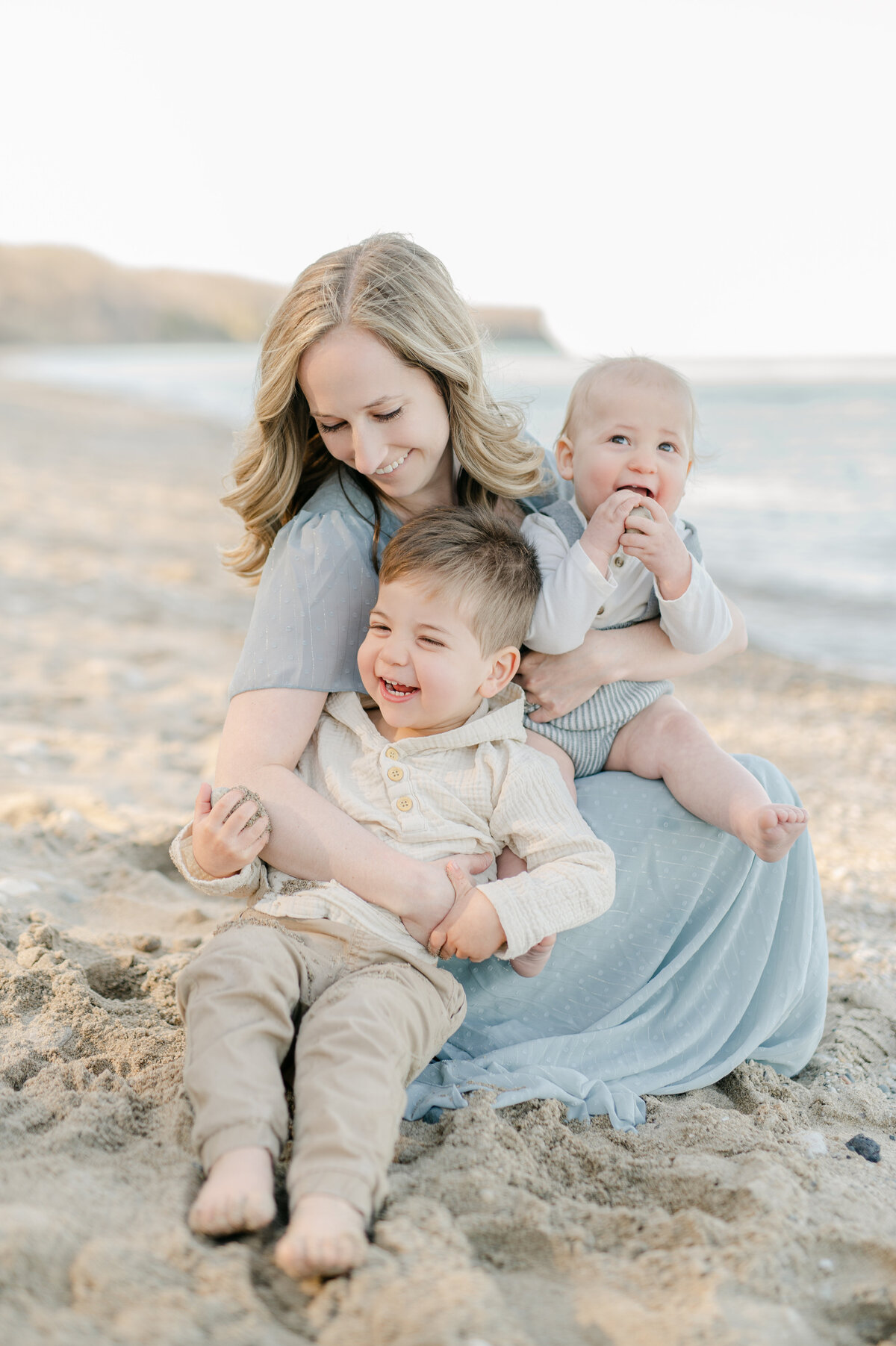 A mom is laughing while holding her two young boys on a beach in Milwaukee