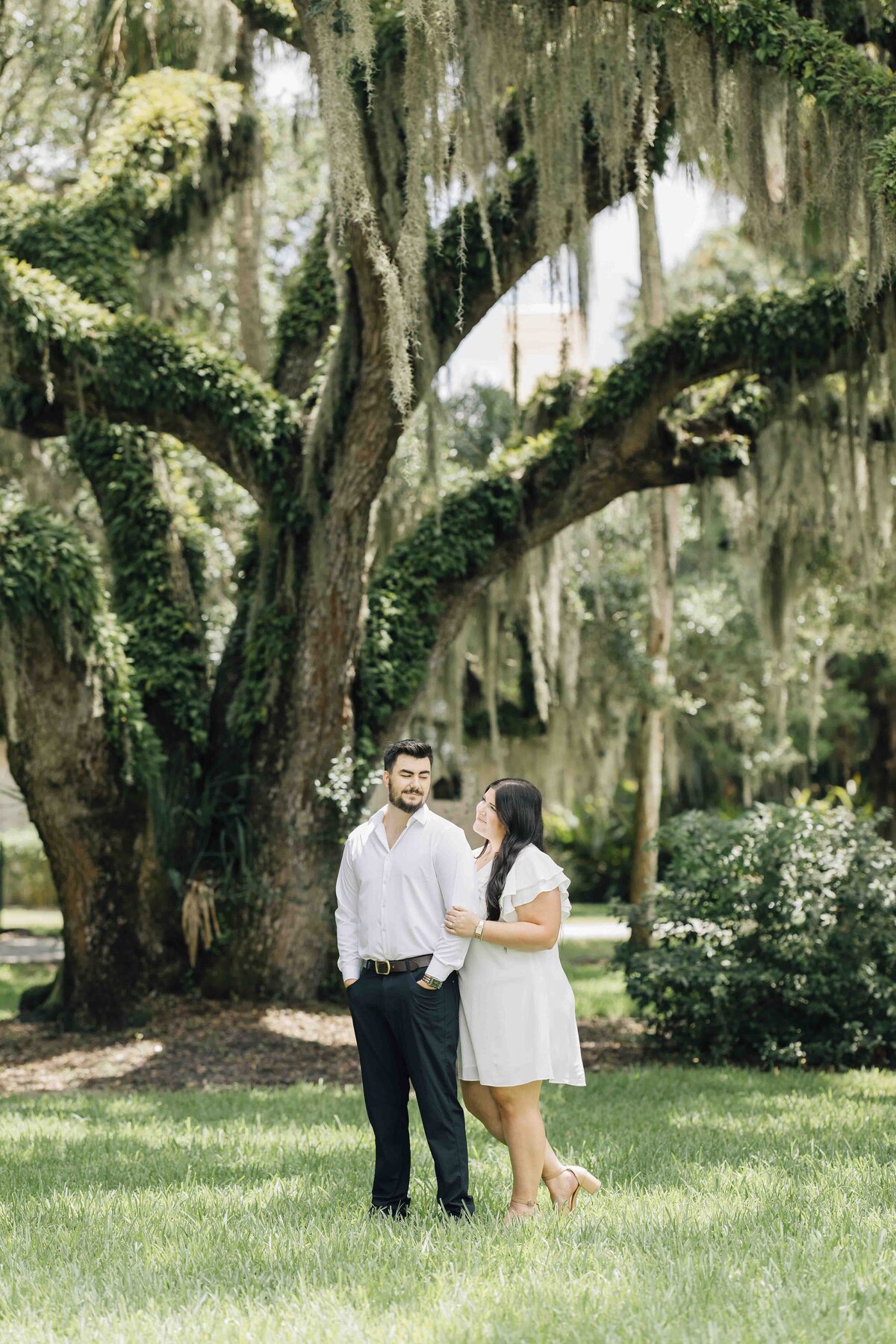 an engaged couple standing under a hanging moss tree
