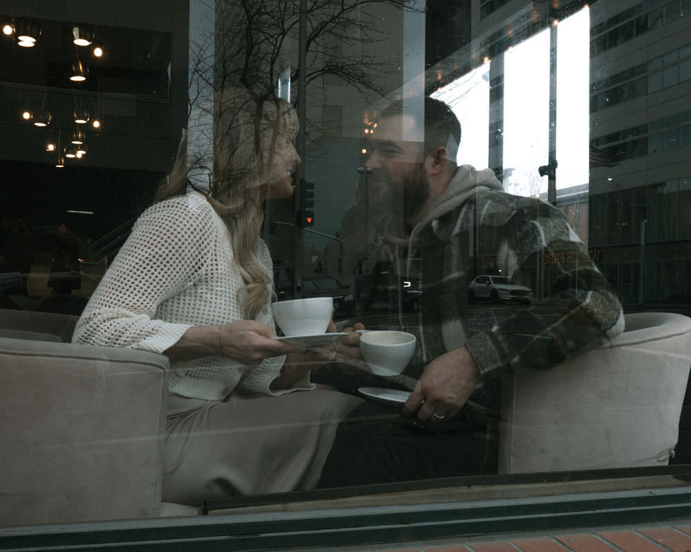 A cofee-loving couple shares a romantic moment among the bookshelves during a library engagement session in Spokane, Washington.