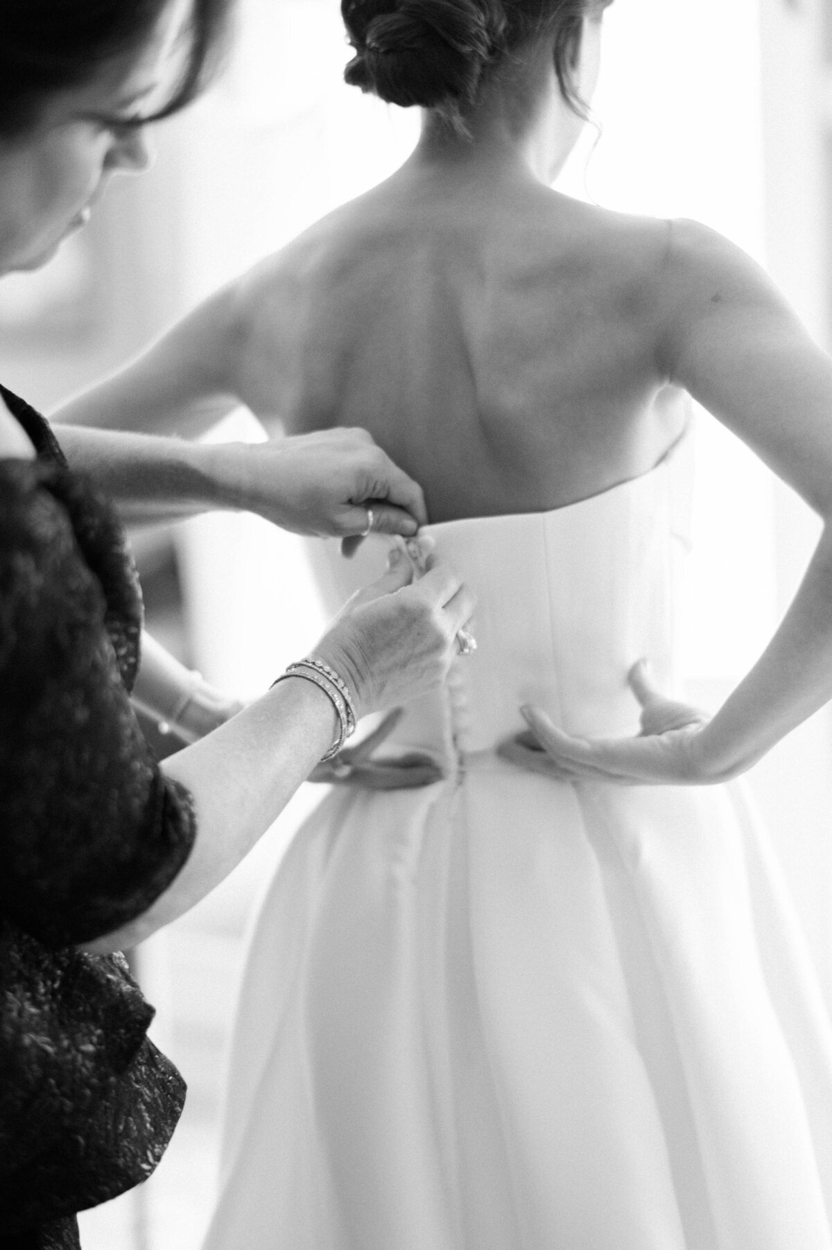 A mother fastening the back of the bride’s strapless gown