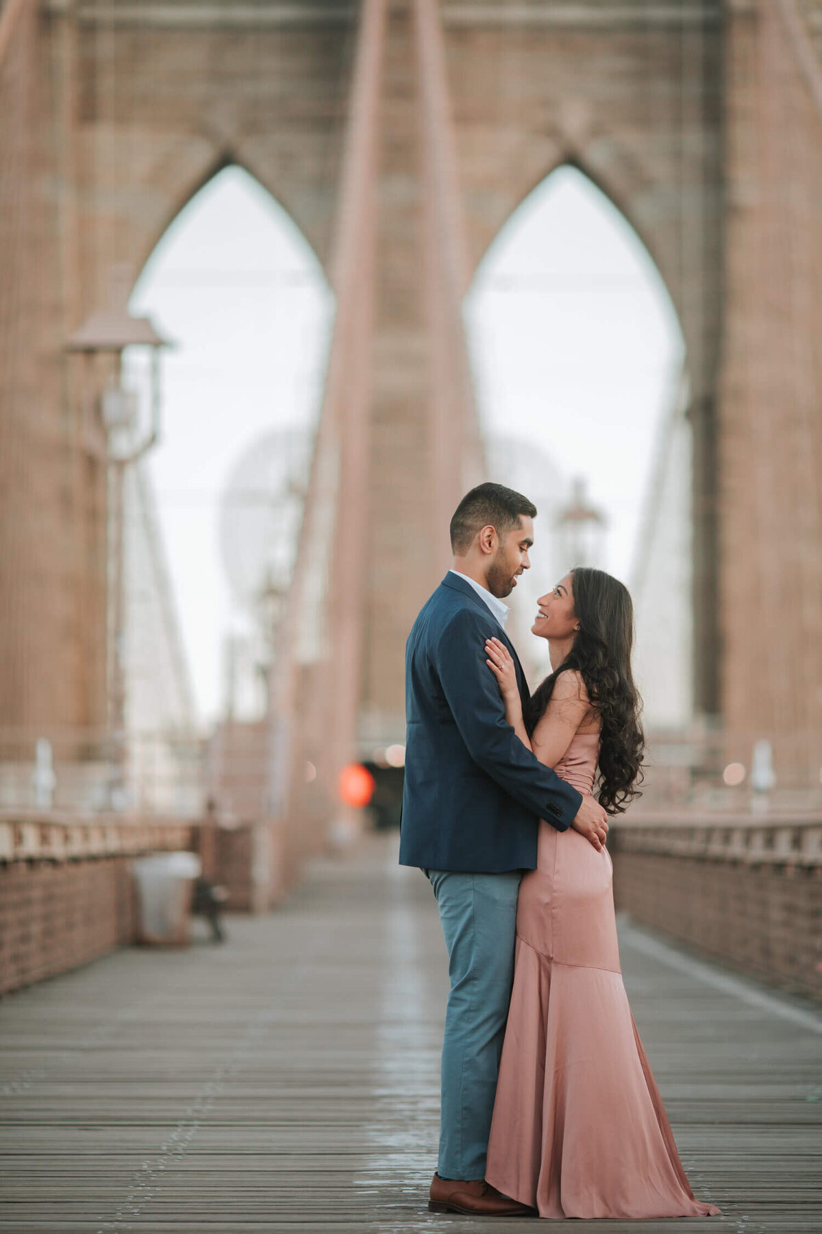 A couple embraces romantically on the Brooklyn Bridge during an engagement session in Brooklyn, New York.