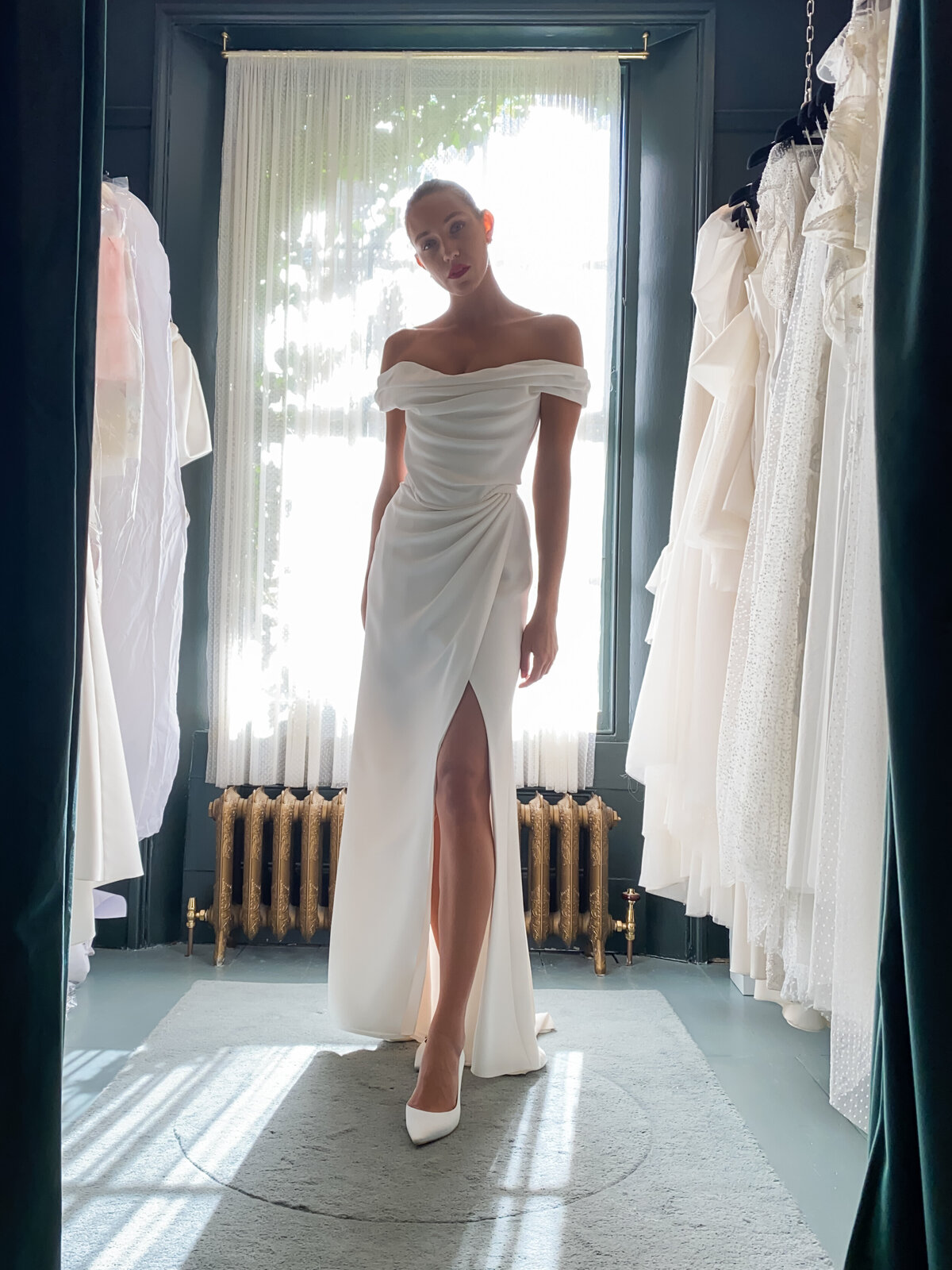 bride wearing white  satin wedding dress in front of window