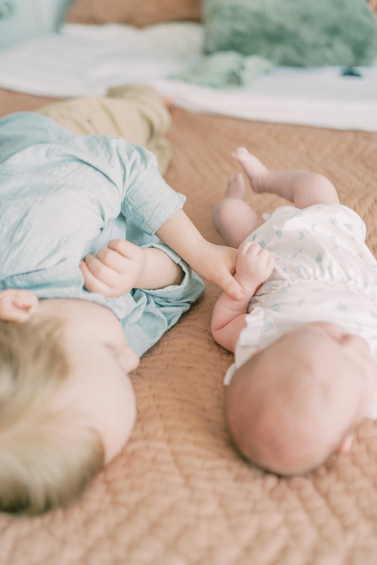 Big brother plays with baby sisters hand as they lay on the bed by Oklahoma City Family Photographer Courtney Cronin