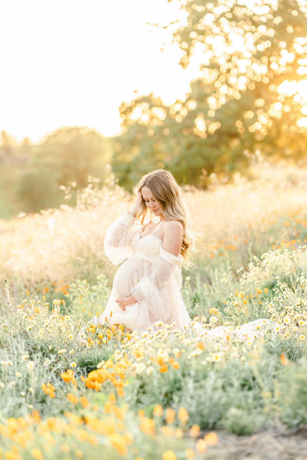 An expecting mother kneels in a field of poppies while caressing her beautiful baby bump photographed by Bay area photographer, Light Livin Photography..