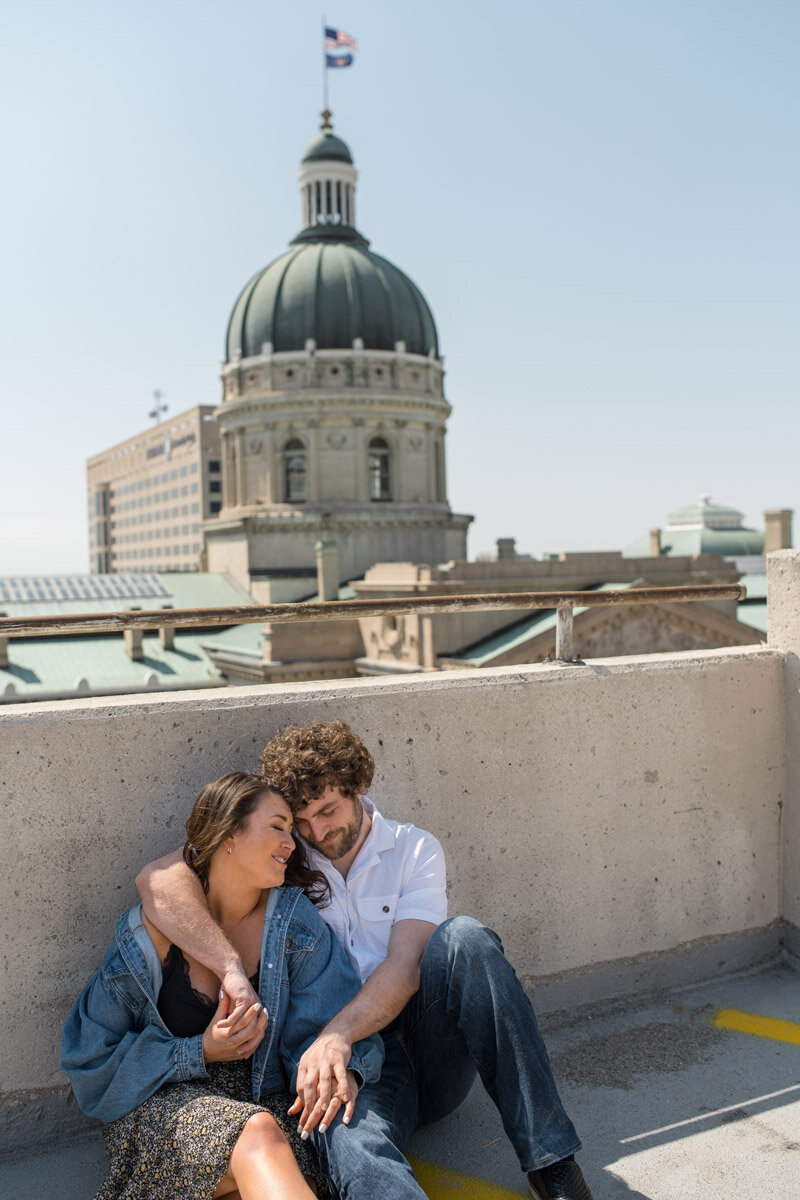 Couple sits snuggling on rooftop parking garage with a view of capital building