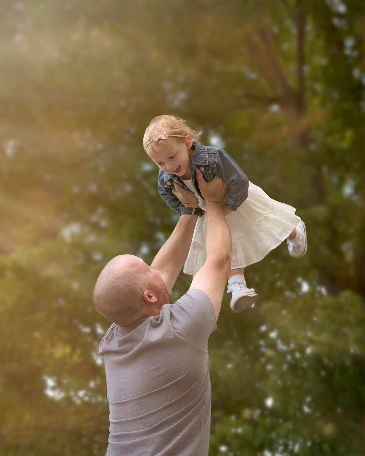 Joyful outdoor family portrait of a father lifting his smiling daughter into the air, captured in Paris, Ontario by Meraki Photographic Creations. Taken at Bronte Provincial Park in Oakville, Ontario.