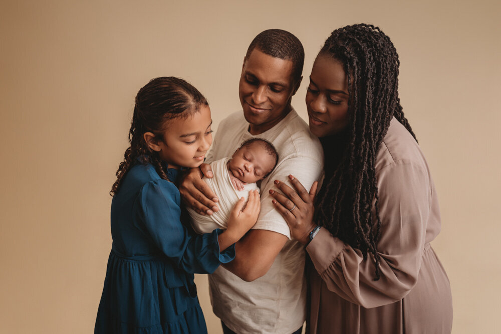 Newborn photos with Atlanta, Georgia newborn photographer of sleeping baby boy with hands under chin wrapped in cream swaddle being held by his mom, dad and big sister.