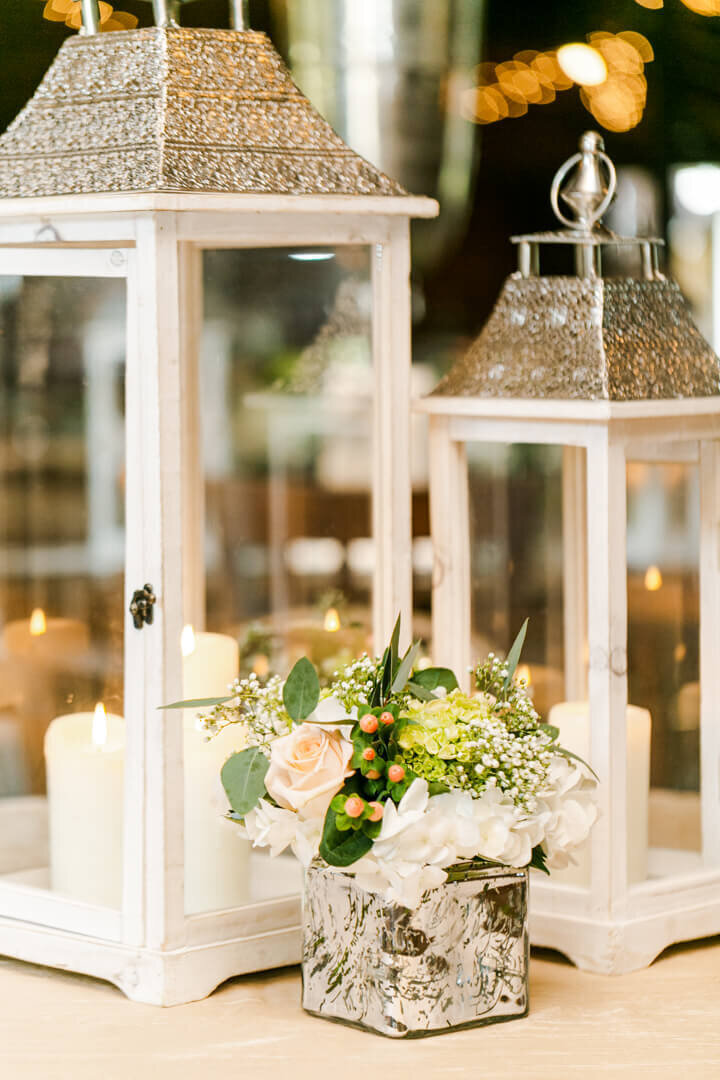 Close up image of white lanterns with candles and flowers in a vase at a wedding reception.