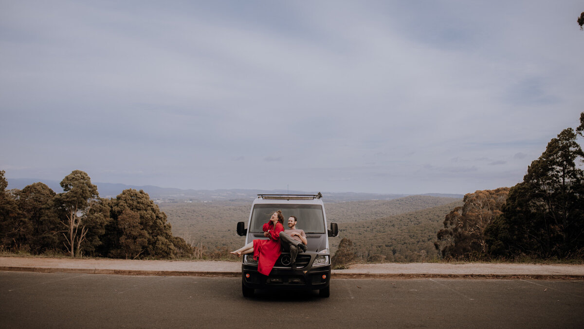 Couple sitting on the hood of a van in front of  a yarra valley landscape