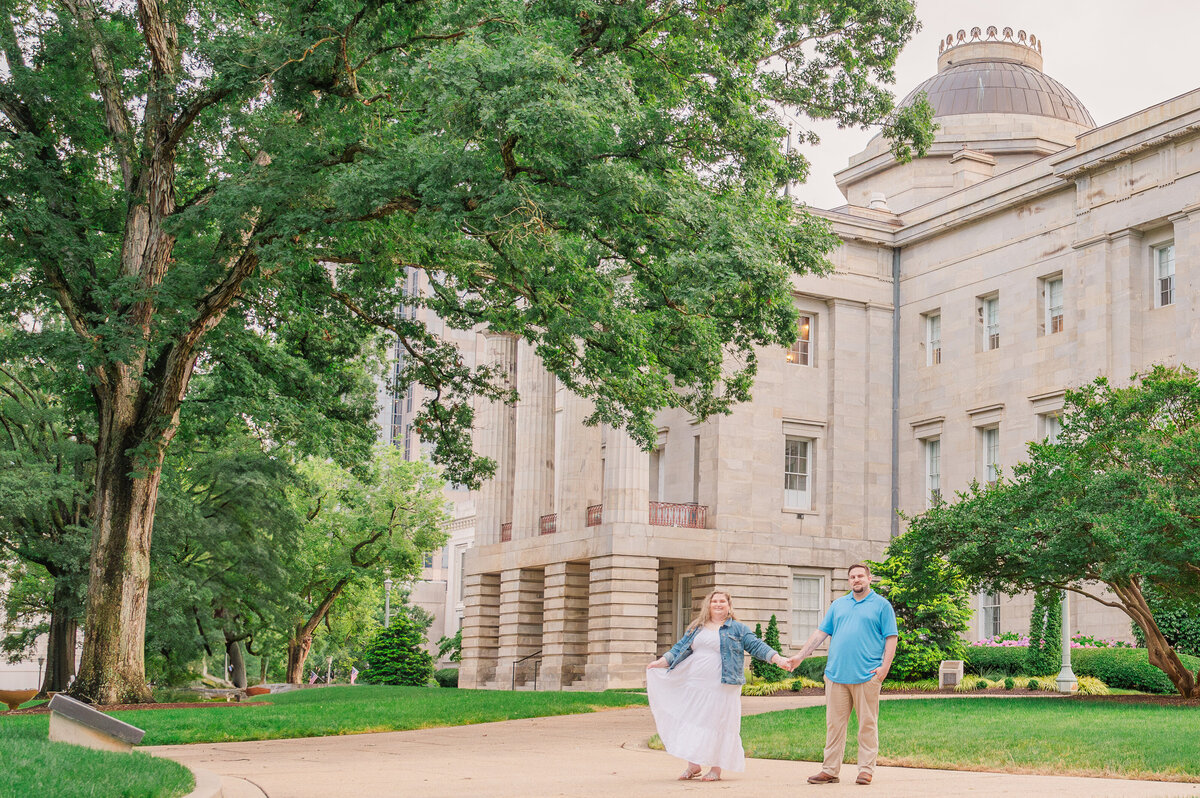 A loving engaged couple holding hands in front of the Raleigh capitol building enjoying their destination wedding photos