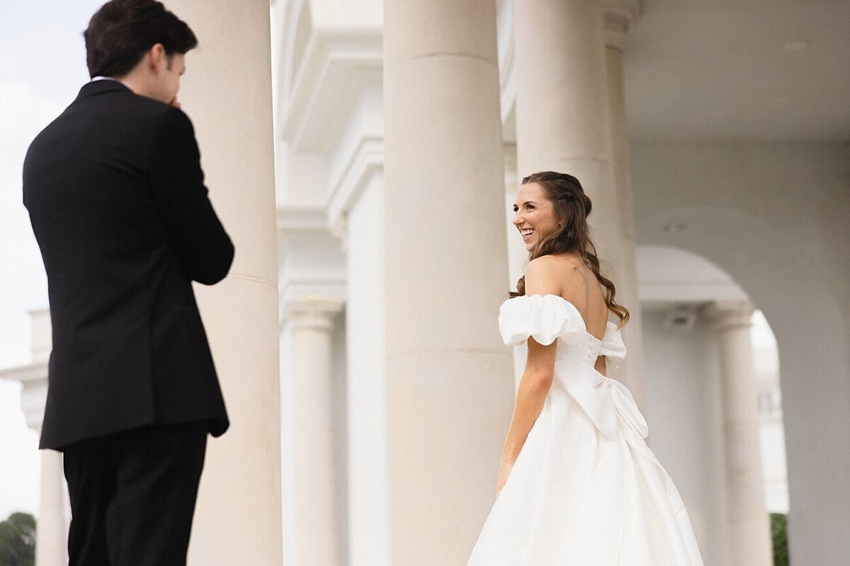Bride showing the groom her dress in front of columns