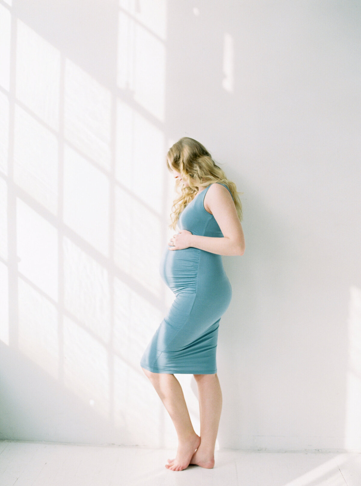 studio maternity photos of a mother in a blue form fitting dress with hand on bump captuered by Seattle Maternity Photographer