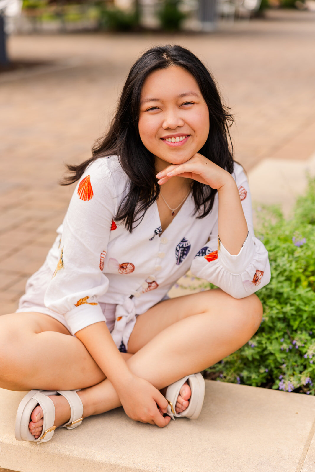 teenage girl sitting legs crossed resting her head on her hand during senior photoshoot in Sandy Spring in a pedestrian street