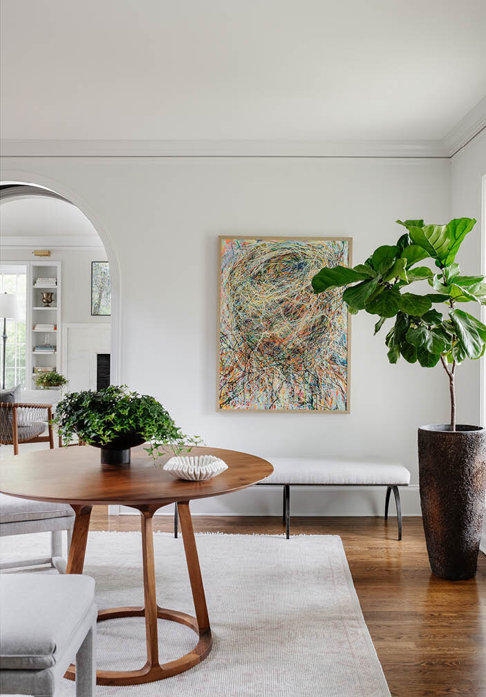 Explore another view of the elegant foyer in a Hingham farmhouse, showcasing a mid-century walnut table, stylish benches, a neutral rug, and custom art on gallery-like walls.