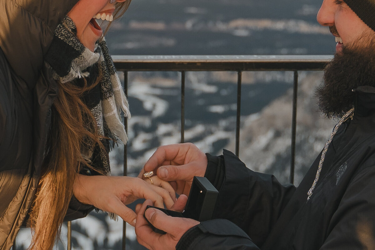 Woman smiles joyfully after placing engagement ring on finger.