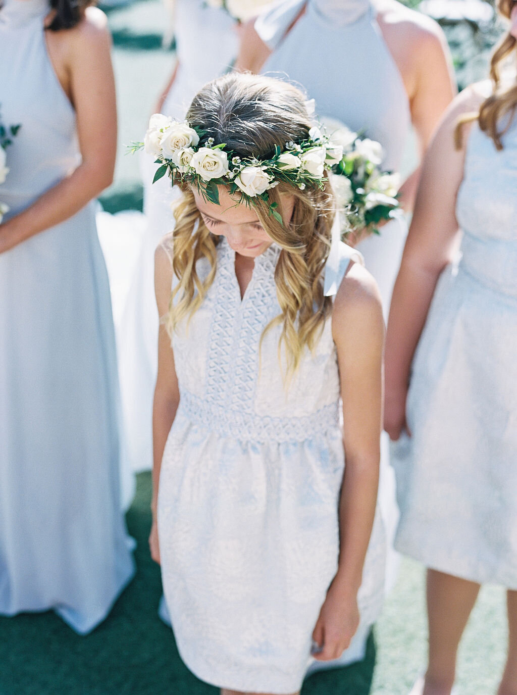A sweet flower girl wearing a delicate white floral crown, captured in a candid moment. This whimsical wedding detail adds a touch of innocence and charm to a breathtaking wedding day.