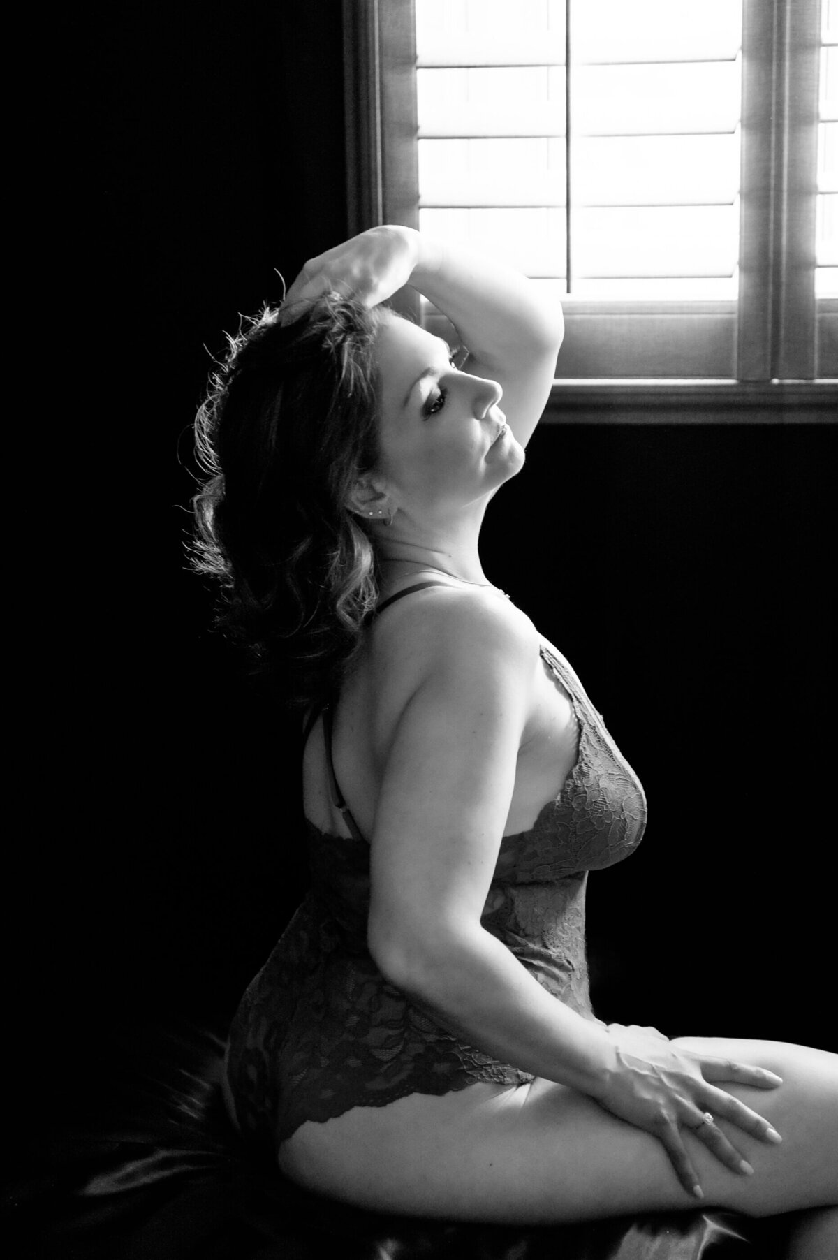 black and white photo of a woman sitting on a bed for her boudoir session.