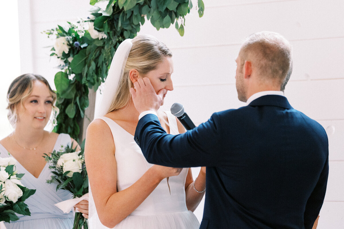 groom is wiping tears from the brides face as she proclaims her vows at Ivory North weddings