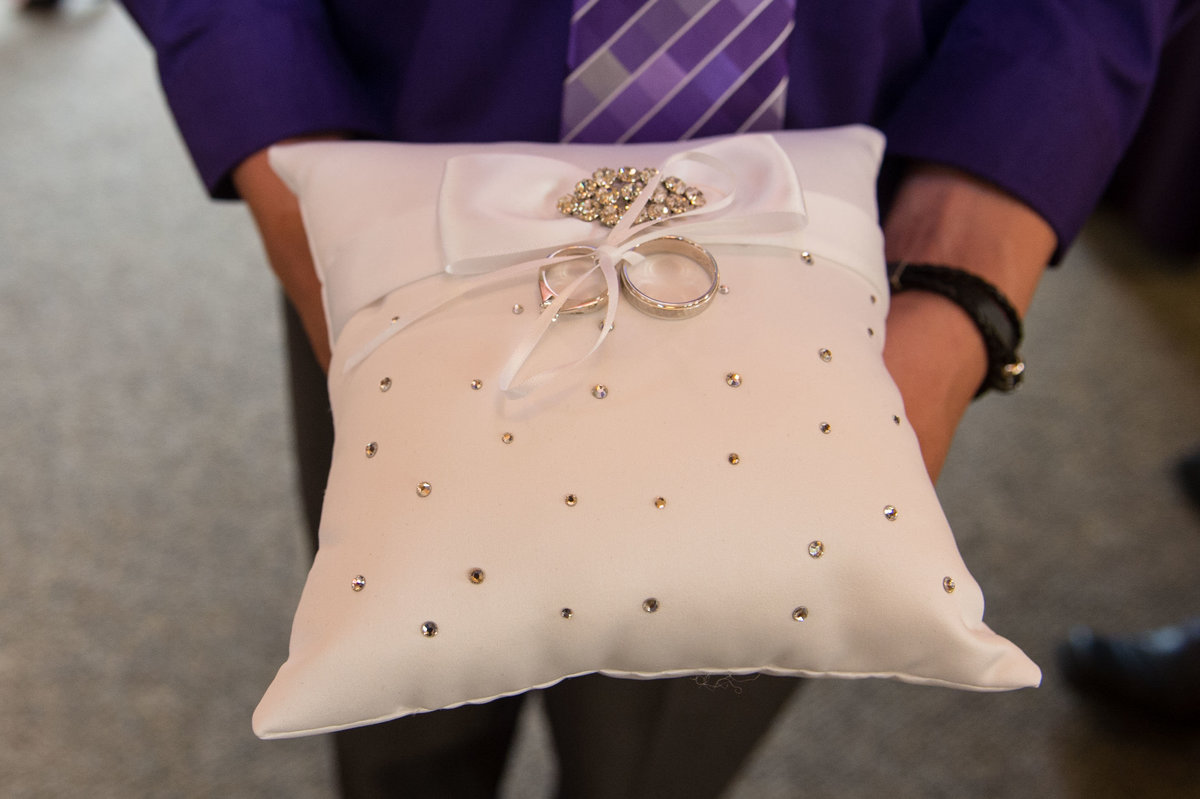 rings laying on pillow held by ring bearer in purple shirt