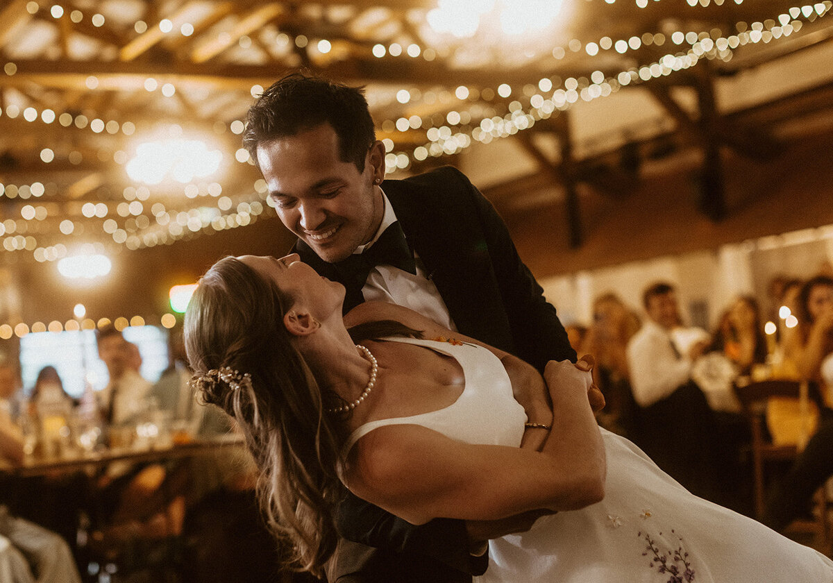 groom dips bride during first dance with twinkle lights