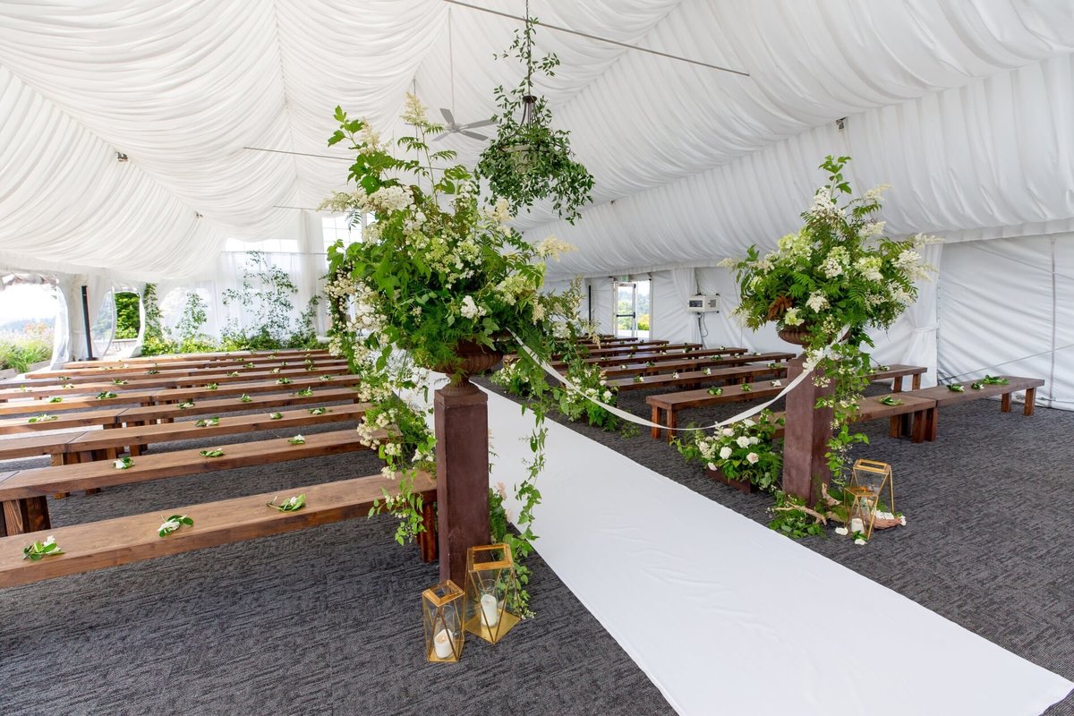 A white aisle runner, large greenery arrangements, gold lanterns at ceremony entrance for wedding at Newcastle golf club