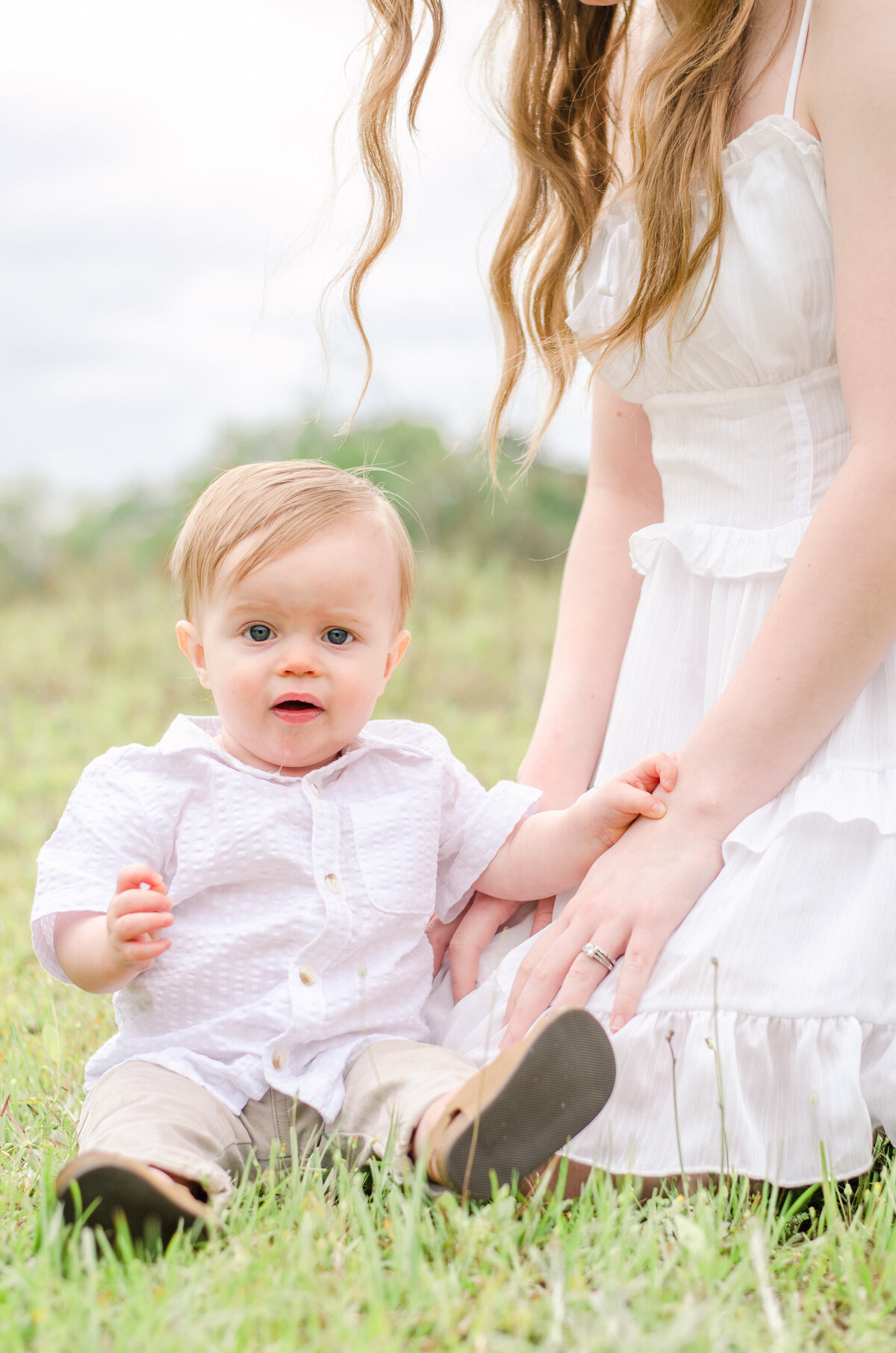 mom kneels while her baby sits in the grass