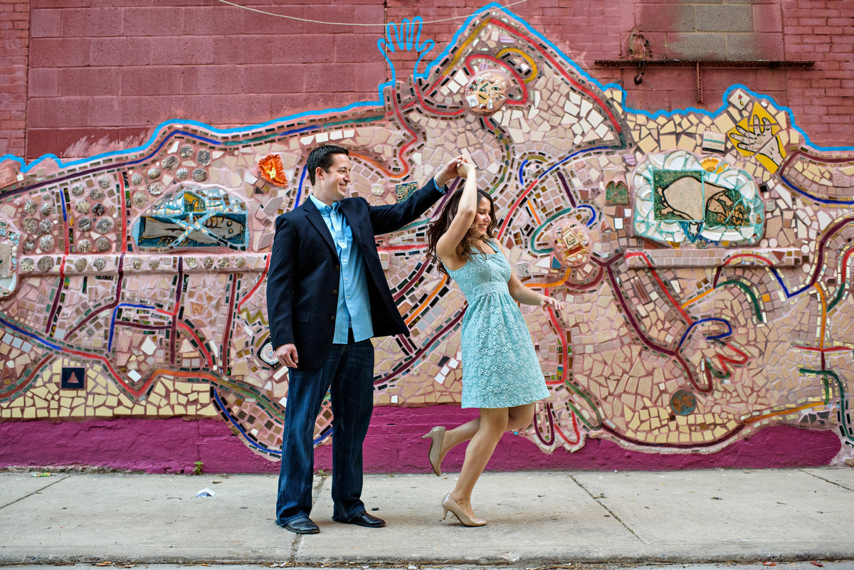 A newly engaged couple dance in front of a south philly mural.