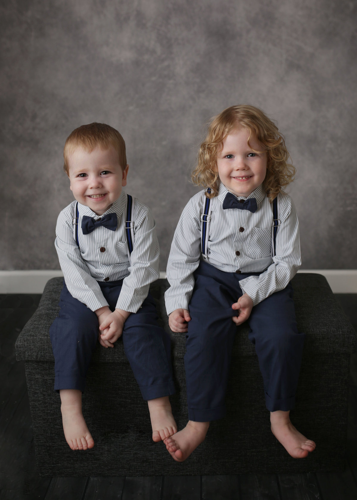 two boys formally dressed with bowties and suspenders sitting on bench