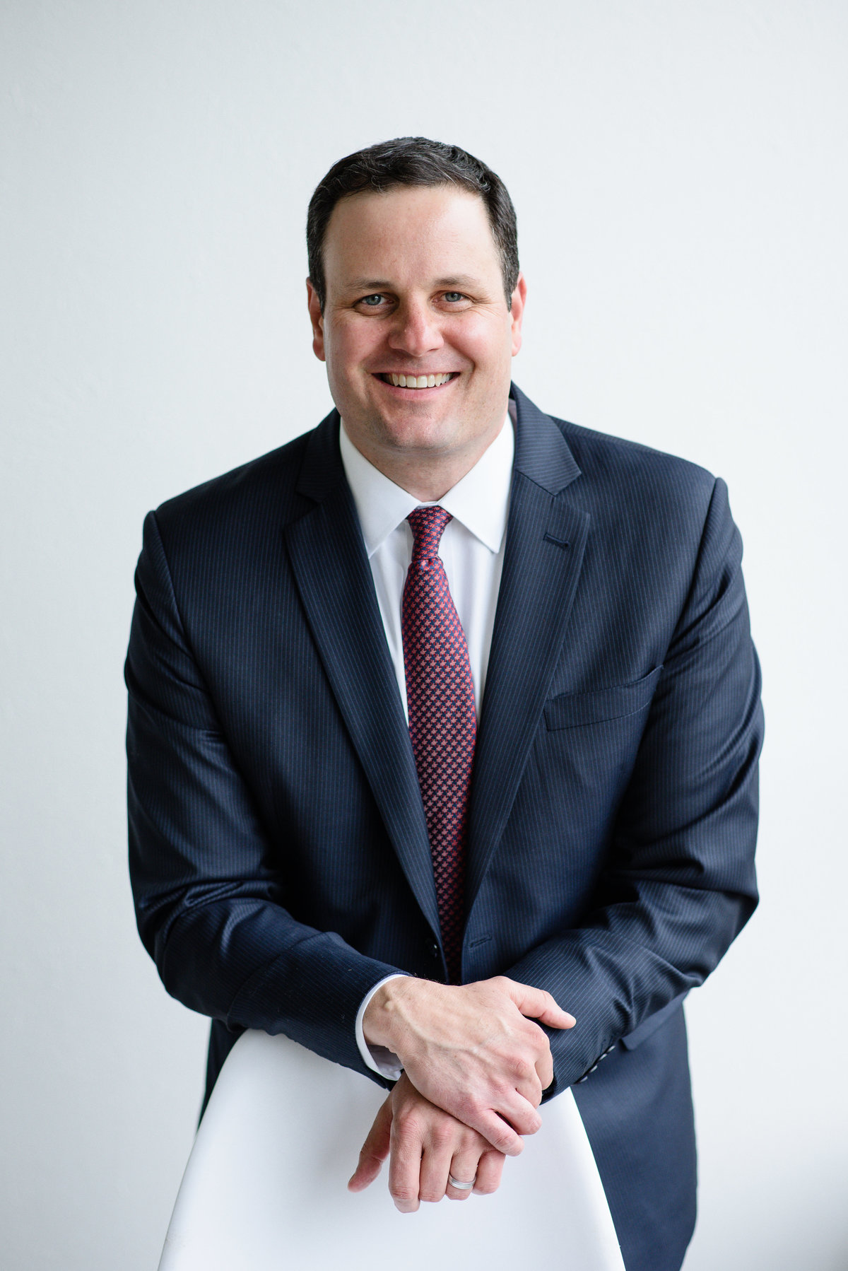 A commercial photographer in denver takes a headshot of a business man in a suit with a red tie leans on a chair for his denver headshots during his branding photos and brand pictures.