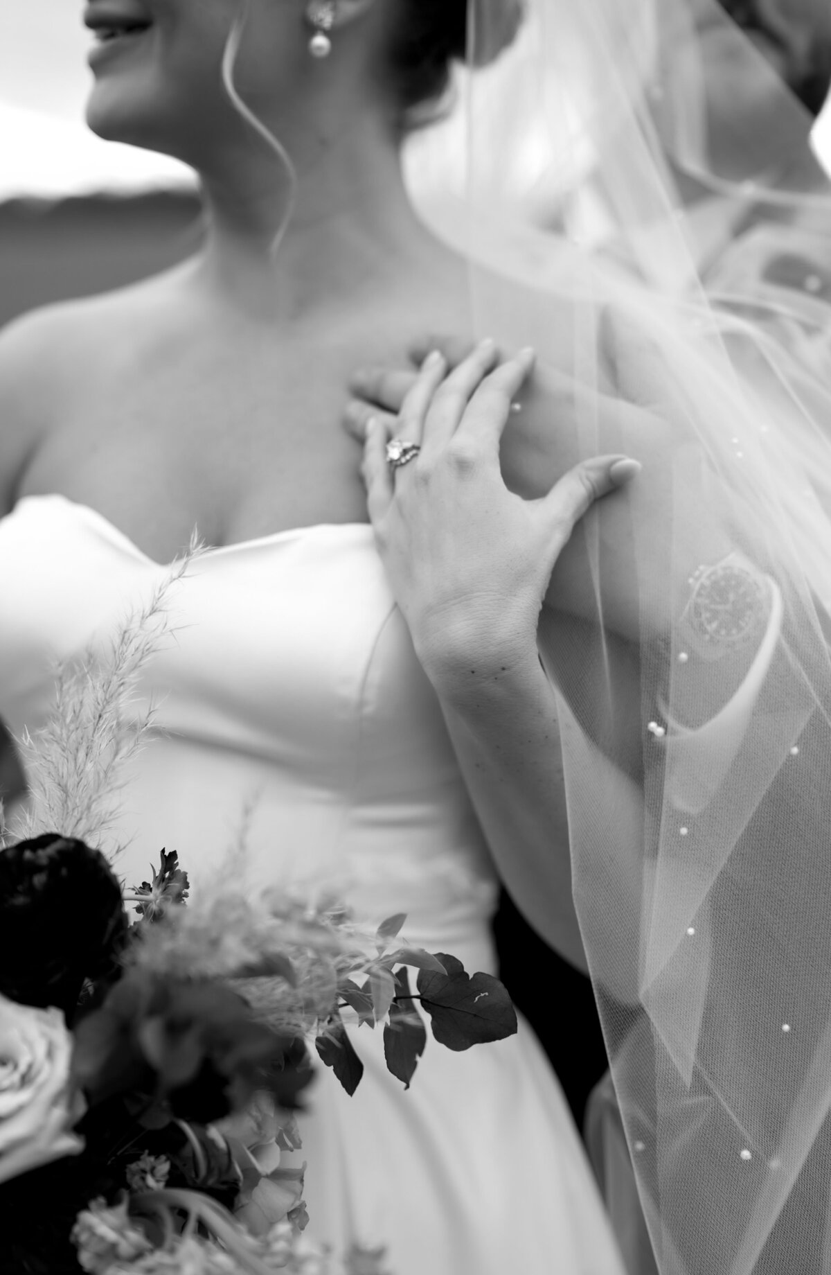 black and white weddin gphotos with groom holding brides shoulder with one hand as she reaches up to touch his hand with the brides veil with pearl beads flowing over photographed by Virginia wedding photographer