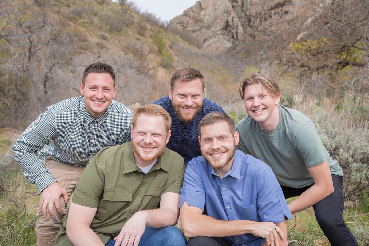 Five brothers weraing blue and green shirts crouching down for a picture with mountain in the background