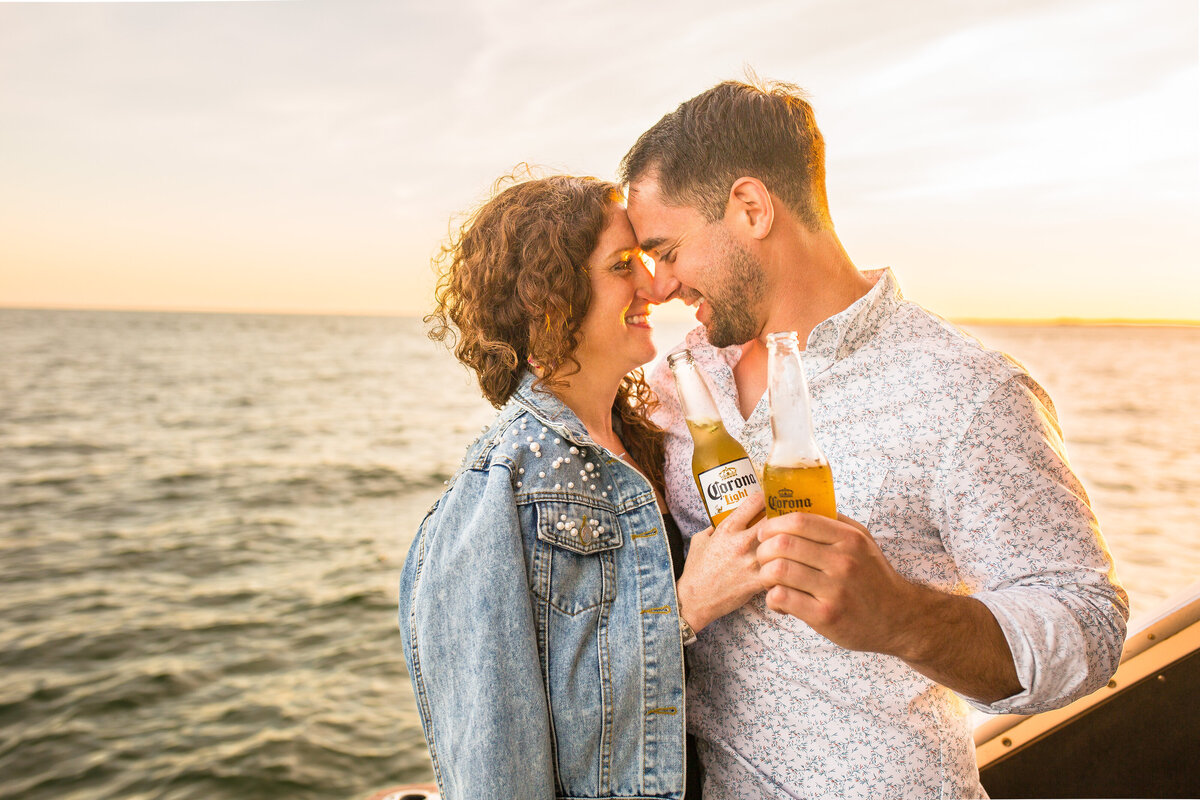 An engaged couple toast beer on a boat during their engagement session.