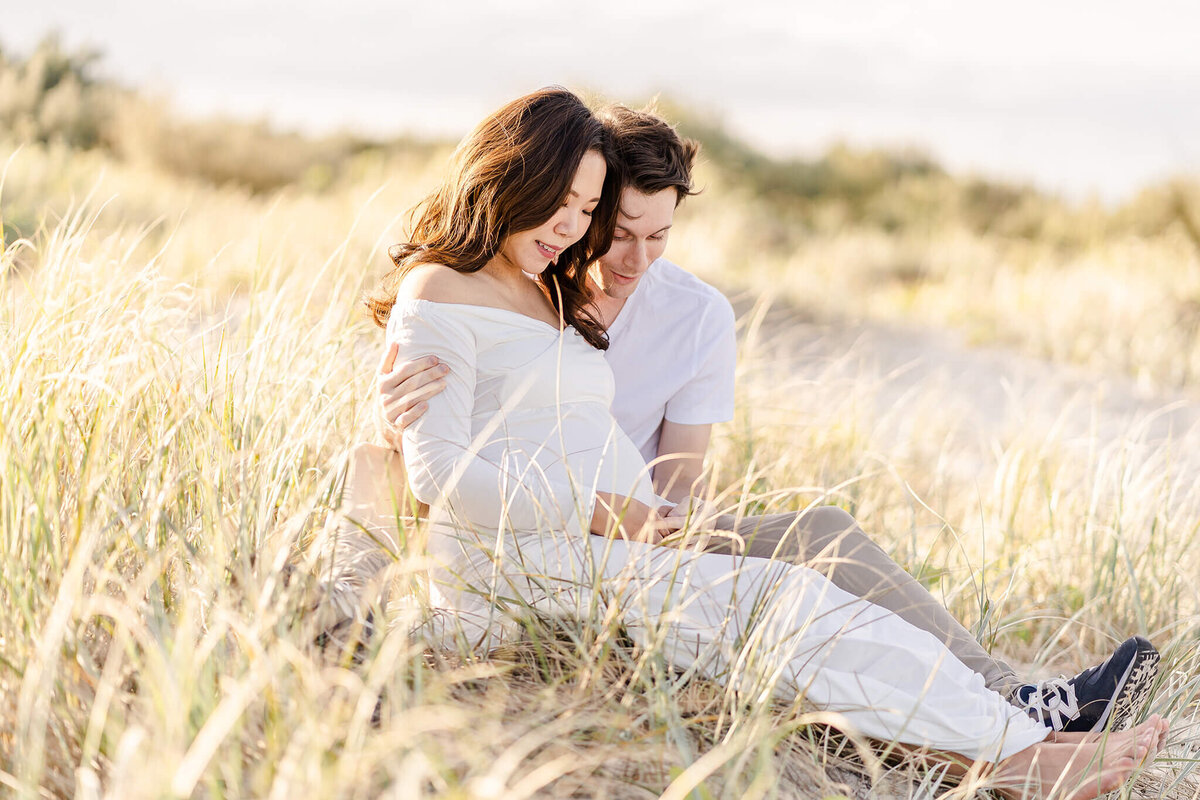 Couple sitting maternity photography pose on golden grass in Gold Coast QLD