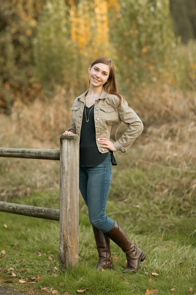 Young woman standing by a fence at a park during fall.