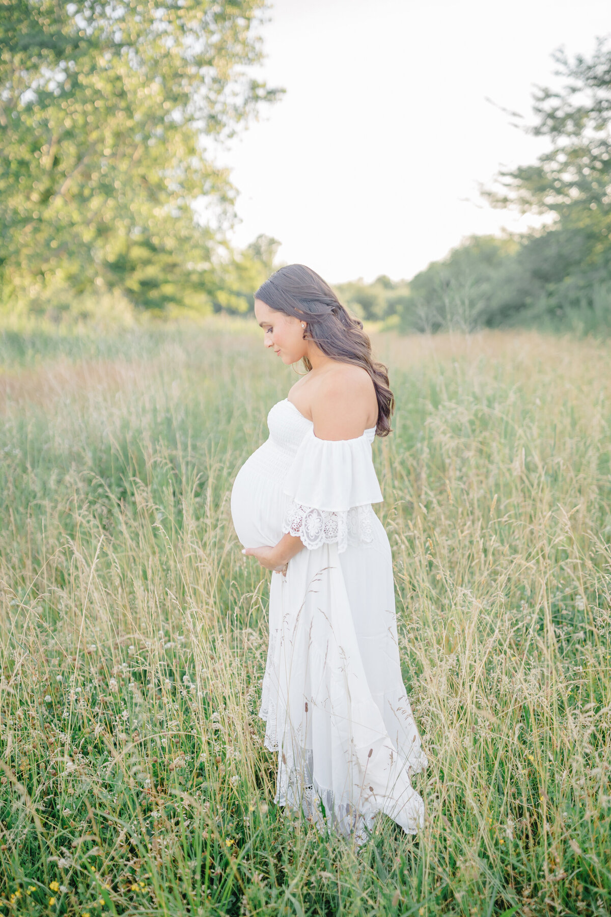 Expecting mother resting in a field of wildflowers, holding her belly with a peaceful smile