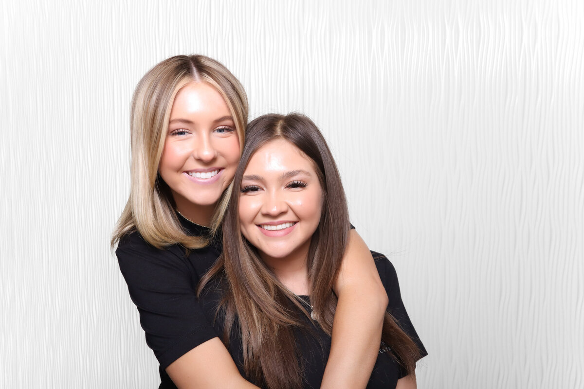 two young women hug for a photo booth picture in their black scrubs