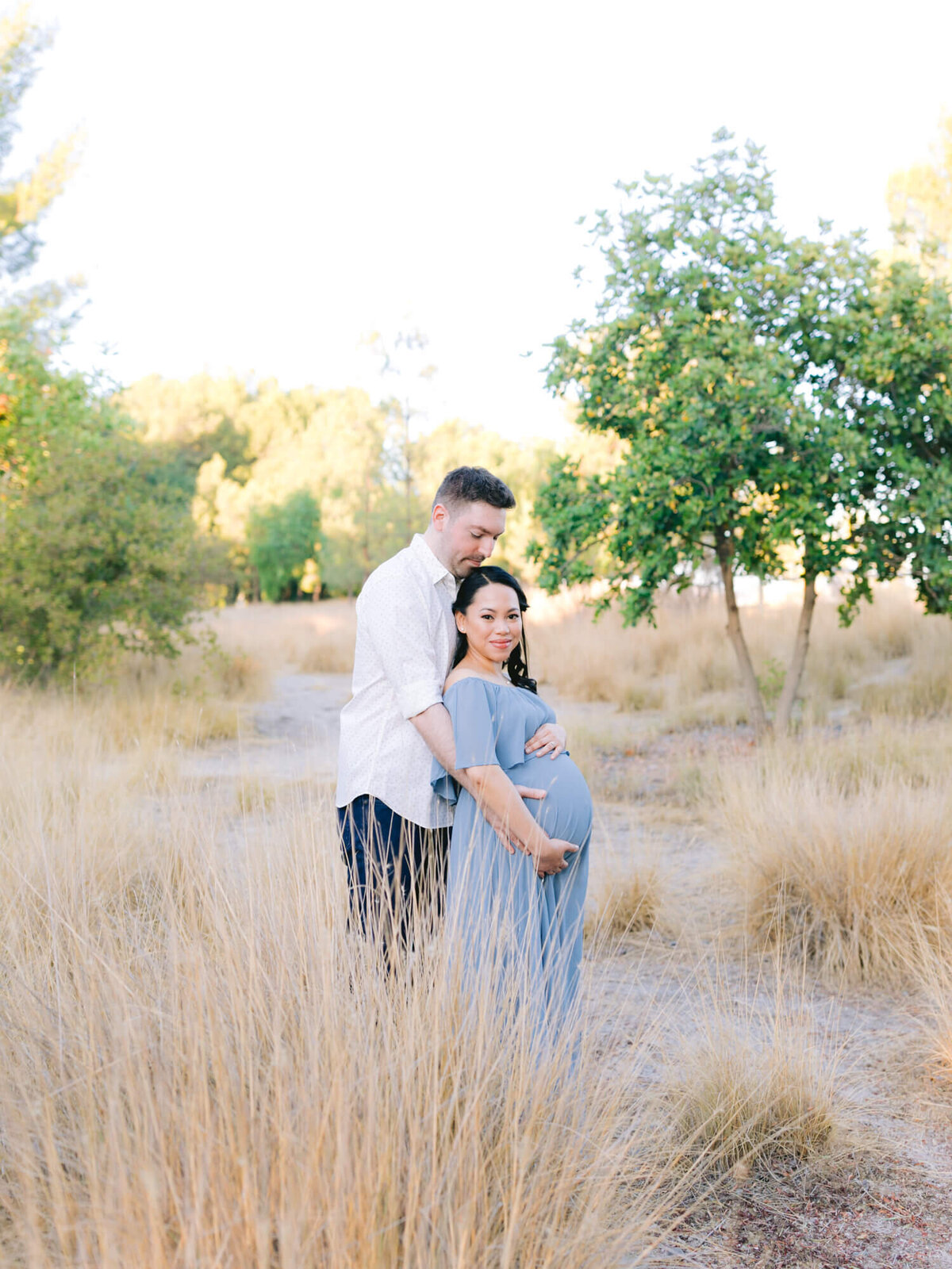 romantic maternity photo of couple wearing blue at yorba linda regional park with fall colors and brown tall grass
