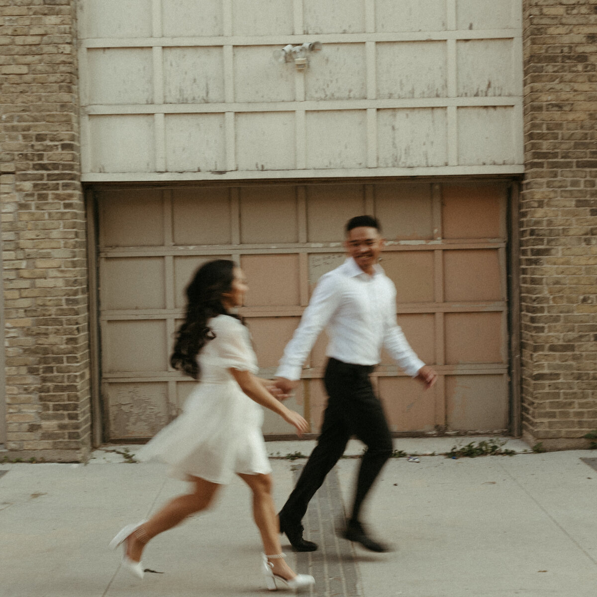 A bride and groom run hand in hand, laughing and looking at each other, capturing a playful and love-filled wedding moment.