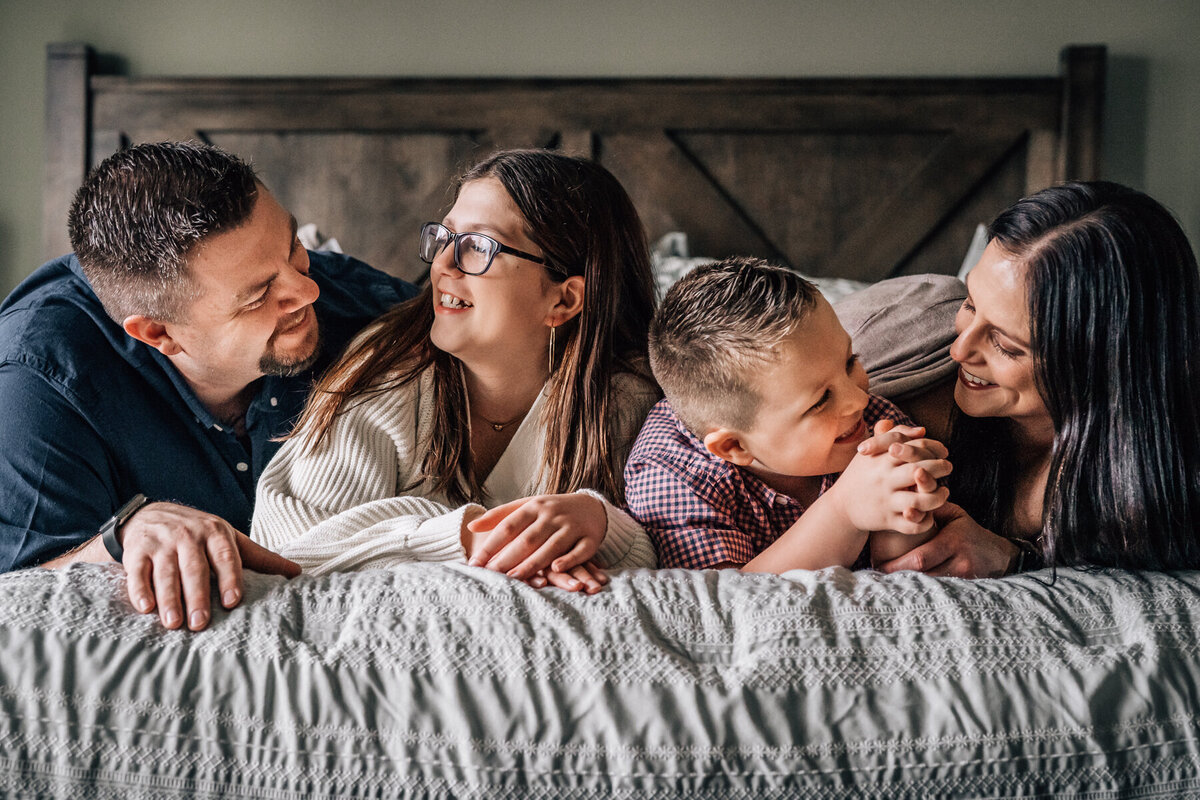 A family lies on their bed and interacts during a family photography session with Minneapolis lifestyle photographer, Kate Simpson.