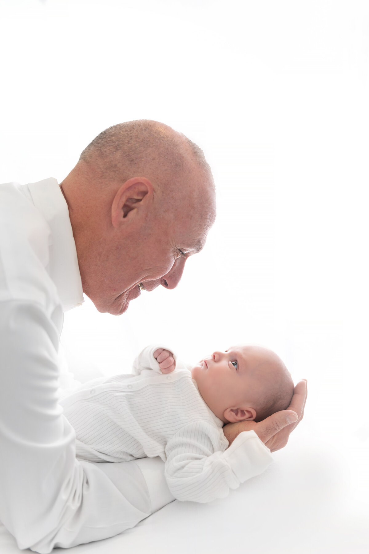 A man in a white shirt smiles down at a newborn baby looking up at him from his arms
