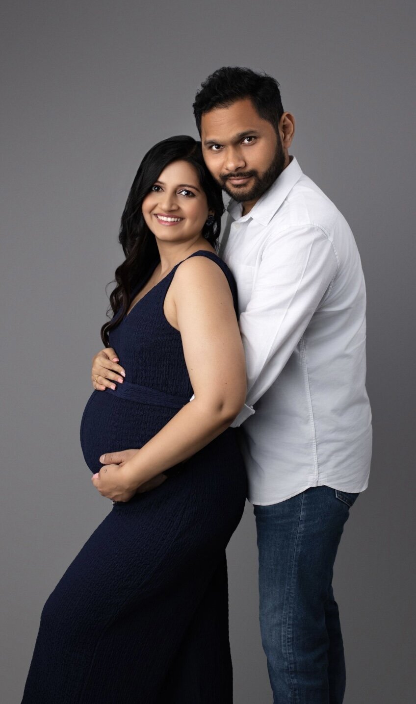 A couple posed for a pregnancy shoot with mom wearing a blue dress and dad wearing a white button down shirt and dark blue jeans.
