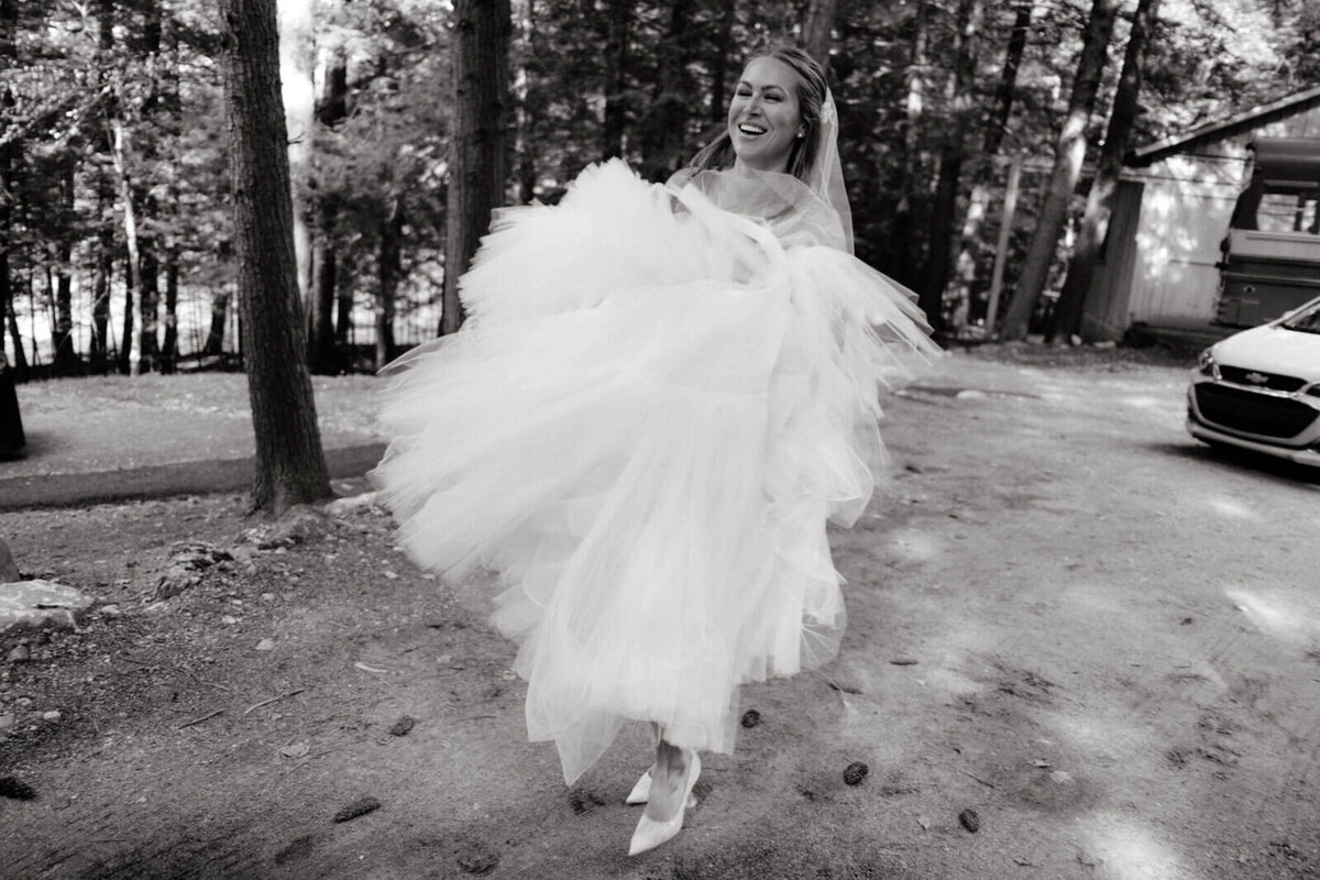 Black and white photo of the bride walking outdoors with a lot of trees at The Ausable Club, New York.